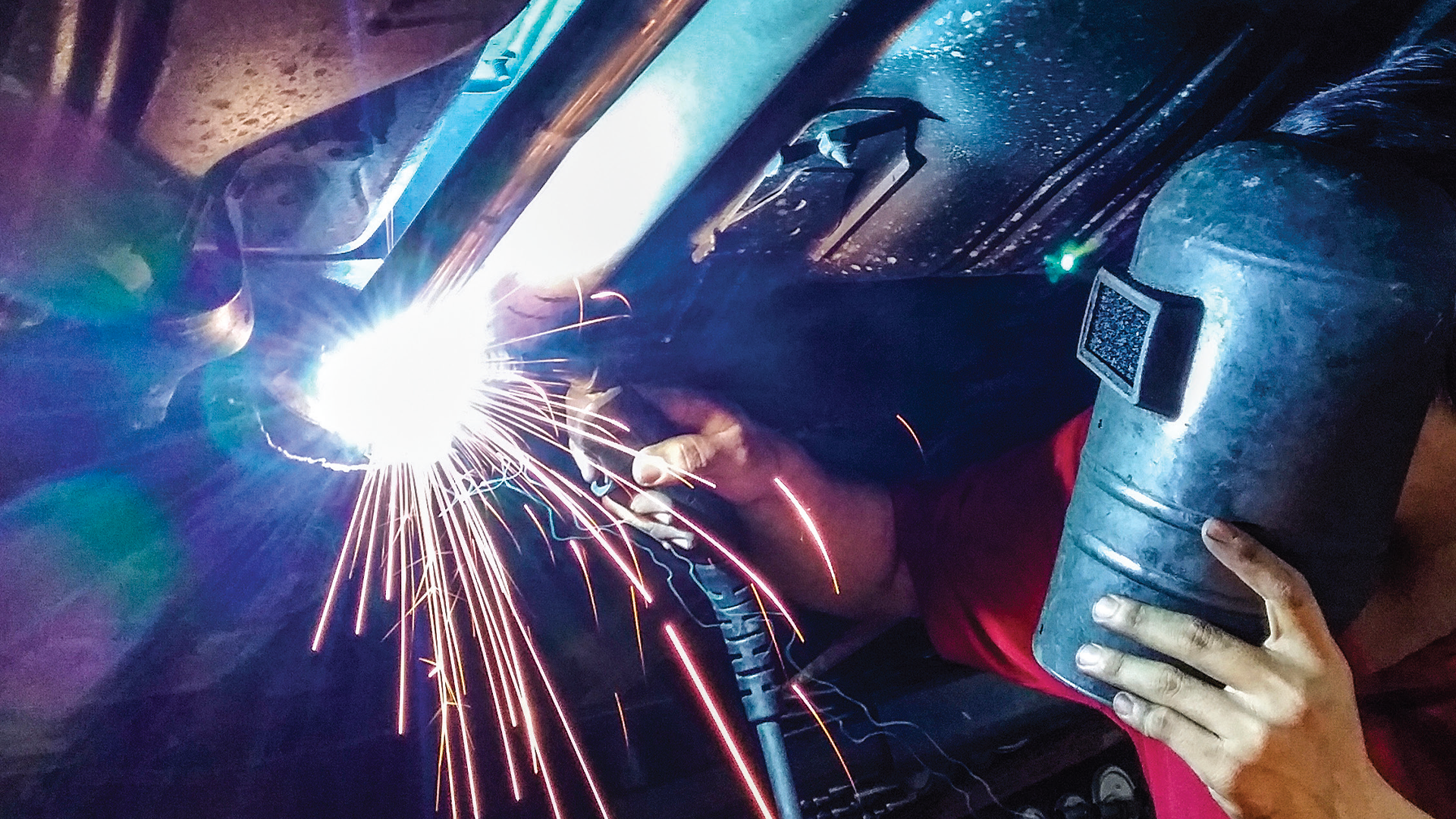 Welder using protective gear creating bright sparks during metal fabrication