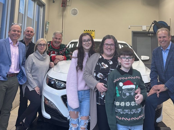 Group of eight people posing with a white vehicle in an indoor showroom