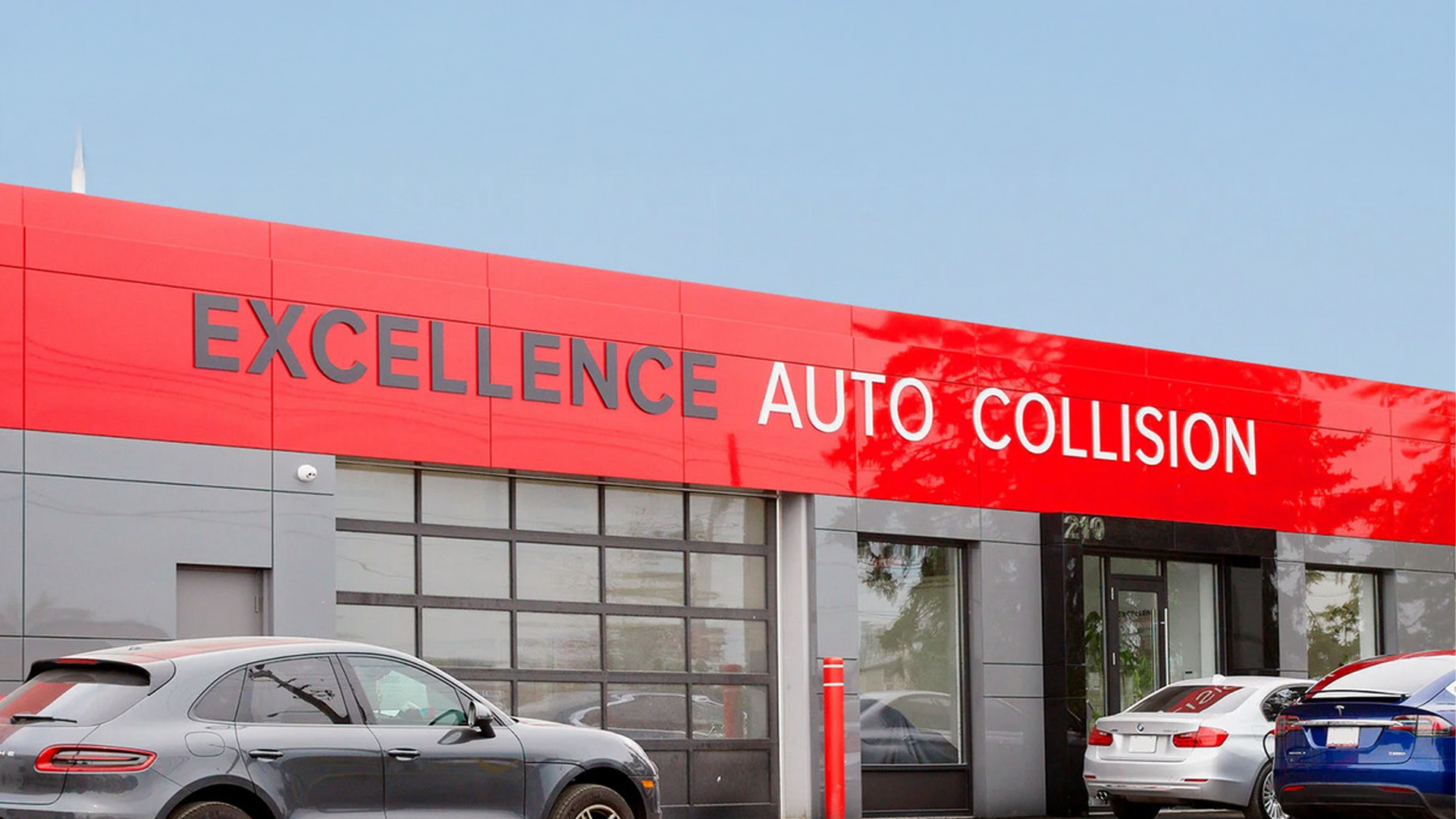 Red and gray Excellence Auto Collision repair shop exterior with parked vehicles
