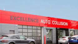 Red and gray Excellence Auto Collision repair shop exterior with parked vehicles