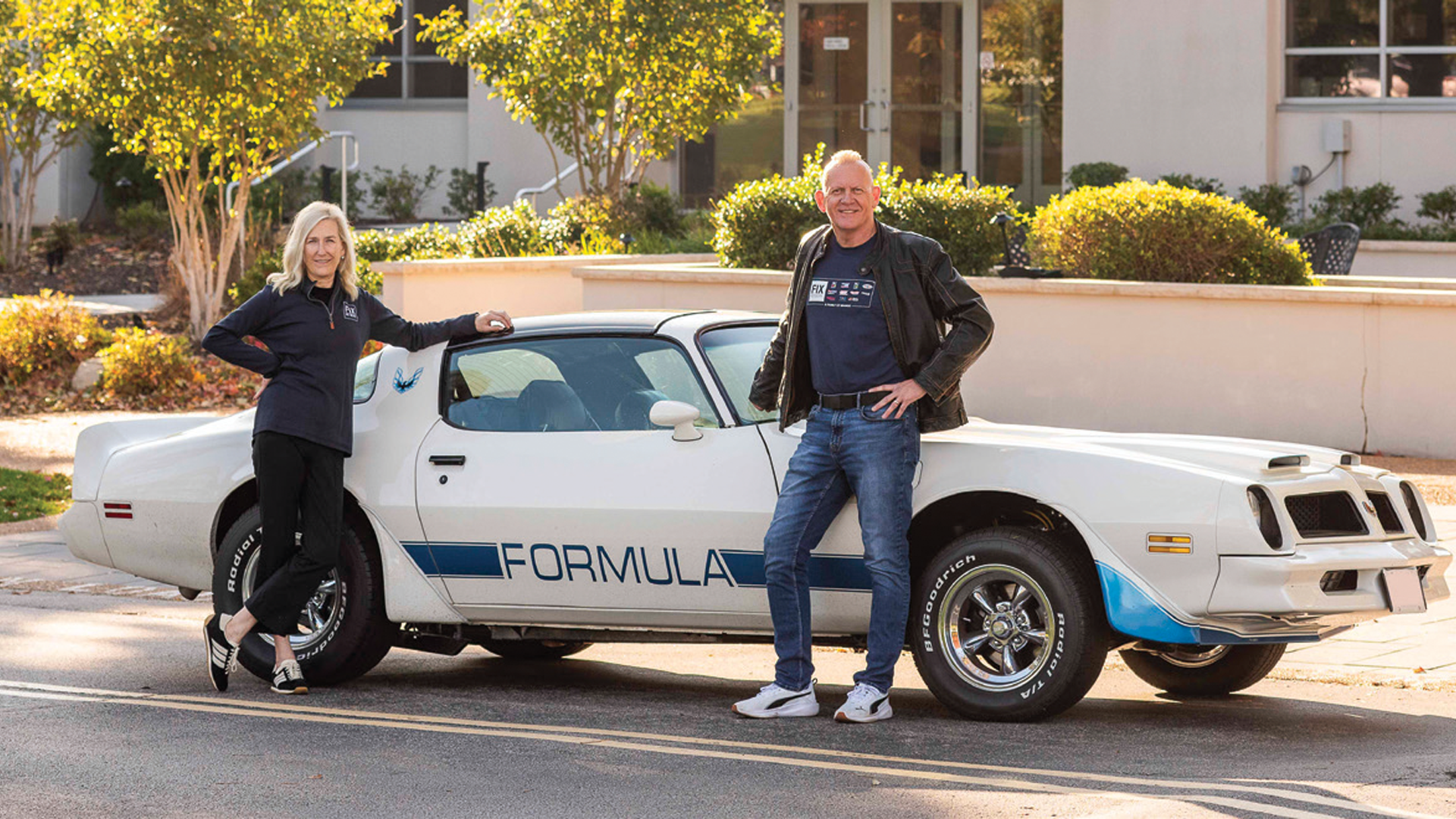 Classic white Pontiac Firebird Formula with two people standing beside it outdoors