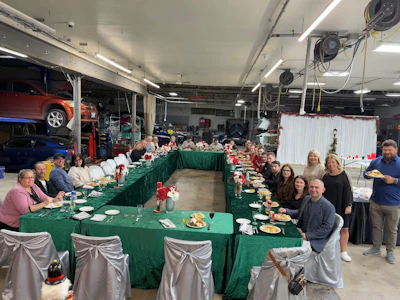 Company holiday lunch in auto repair shop with green-draped tables and cars in background