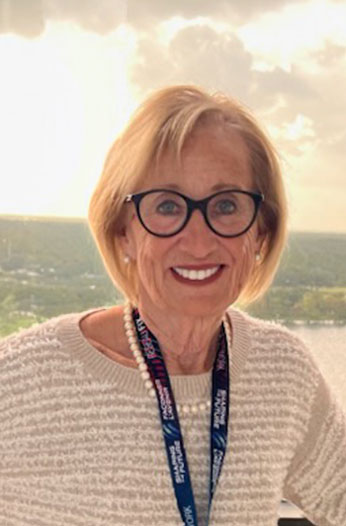 Smiling senior woman in glasses wearing a white sweater and lanyard outdoors
