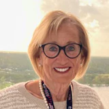 Smiling senior woman in glasses wearing a white sweater and lanyard outdoors