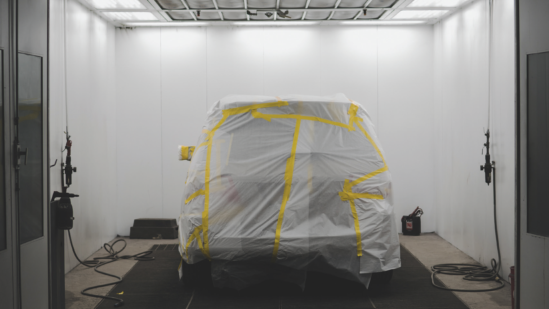 Vehicle draped in white protective sheet with yellow tape in sterile white room