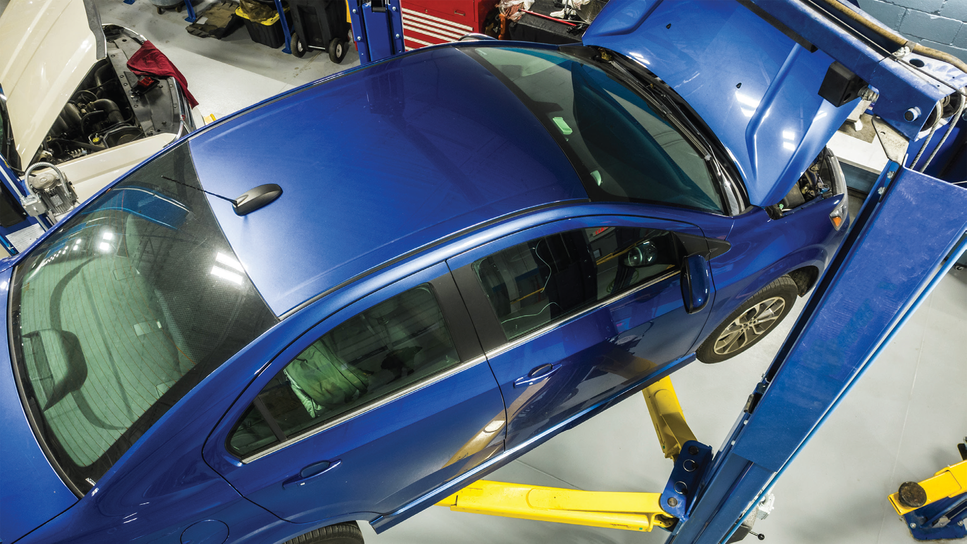 Blue sedan raised on blue automotive lift in repair garage