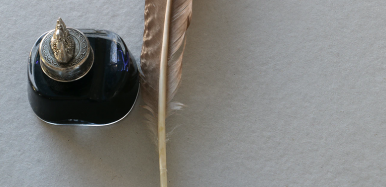 Black ink bottle with ornate lid and vintage feather quill pen