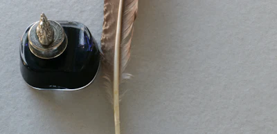Black ink bottle with ornate lid and vintage feather quill pen