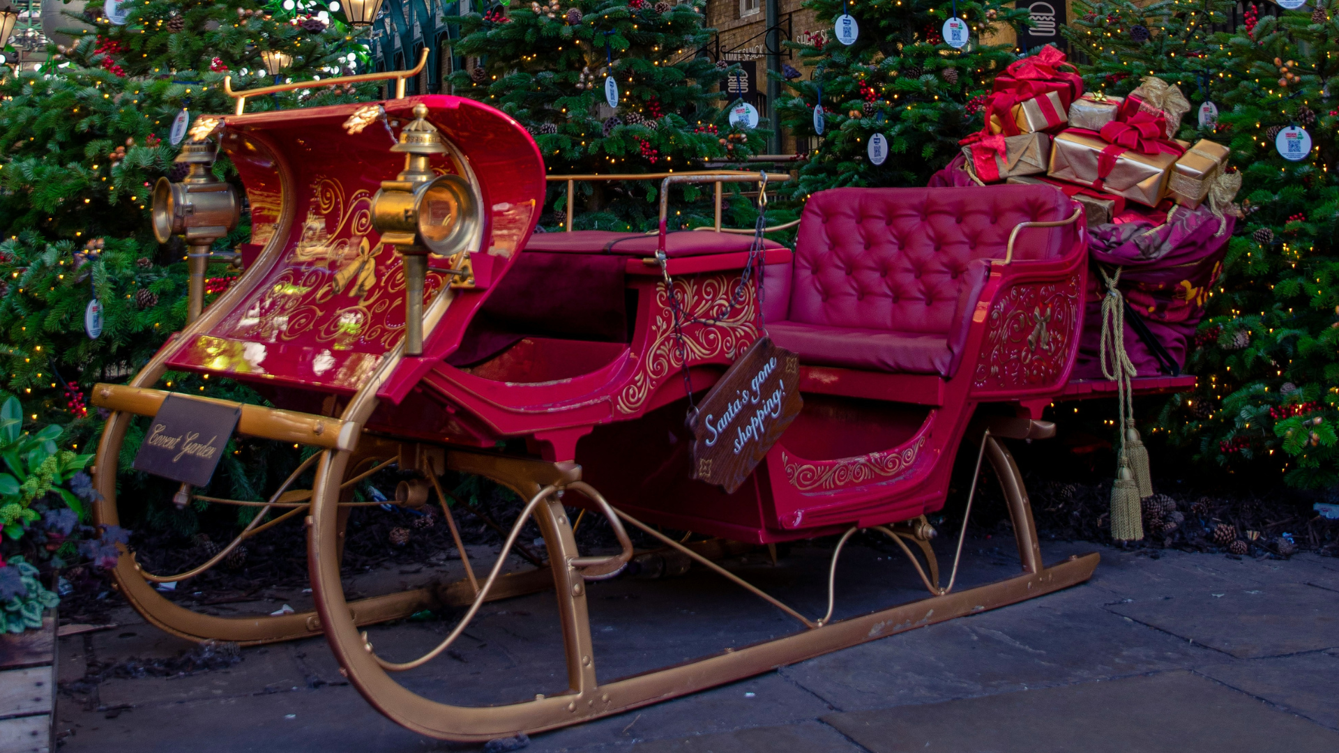 Elegant red vintage Christmas sleigh with ornate gold details, surrounded by Christmas trees
