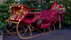 Elegant red vintage Christmas sleigh with ornate gold details, surrounded by Christmas trees