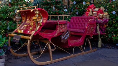 Elegant red vintage Christmas sleigh with ornate gold details, surrounded by Christmas trees
