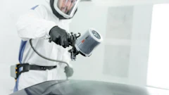 Auto painter in protective gear using spray gun on vehicle surface