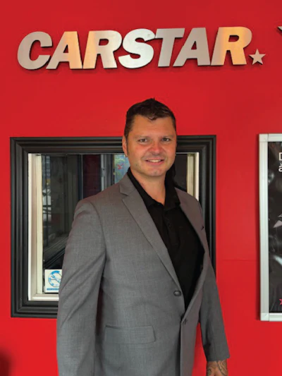 Professional in gray suit standing in front of CARSTAR automotive service center