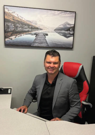 Professional in gray blazer seated at desk with mountain lake landscape art