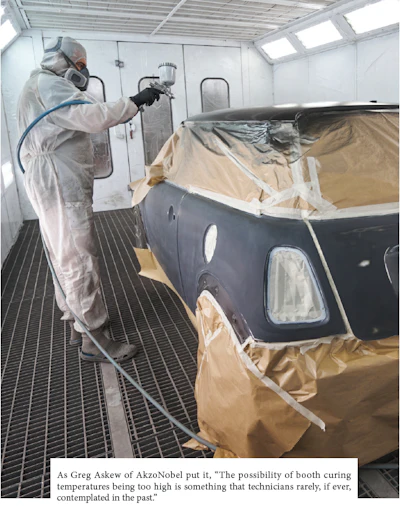 Automotive painter in white protective suit spraying paint on vehicle in spray booth