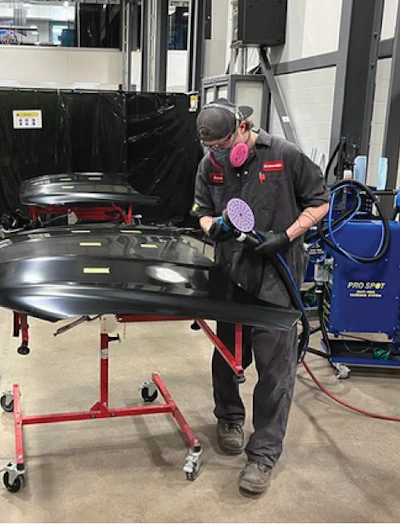 Auto body technician in protective gear sanding vehicle panel in workshop