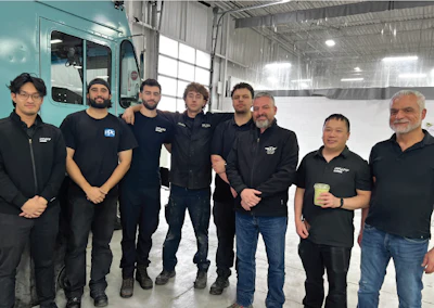 Team of eight workers in black uniforms standing together in industrial warehouse