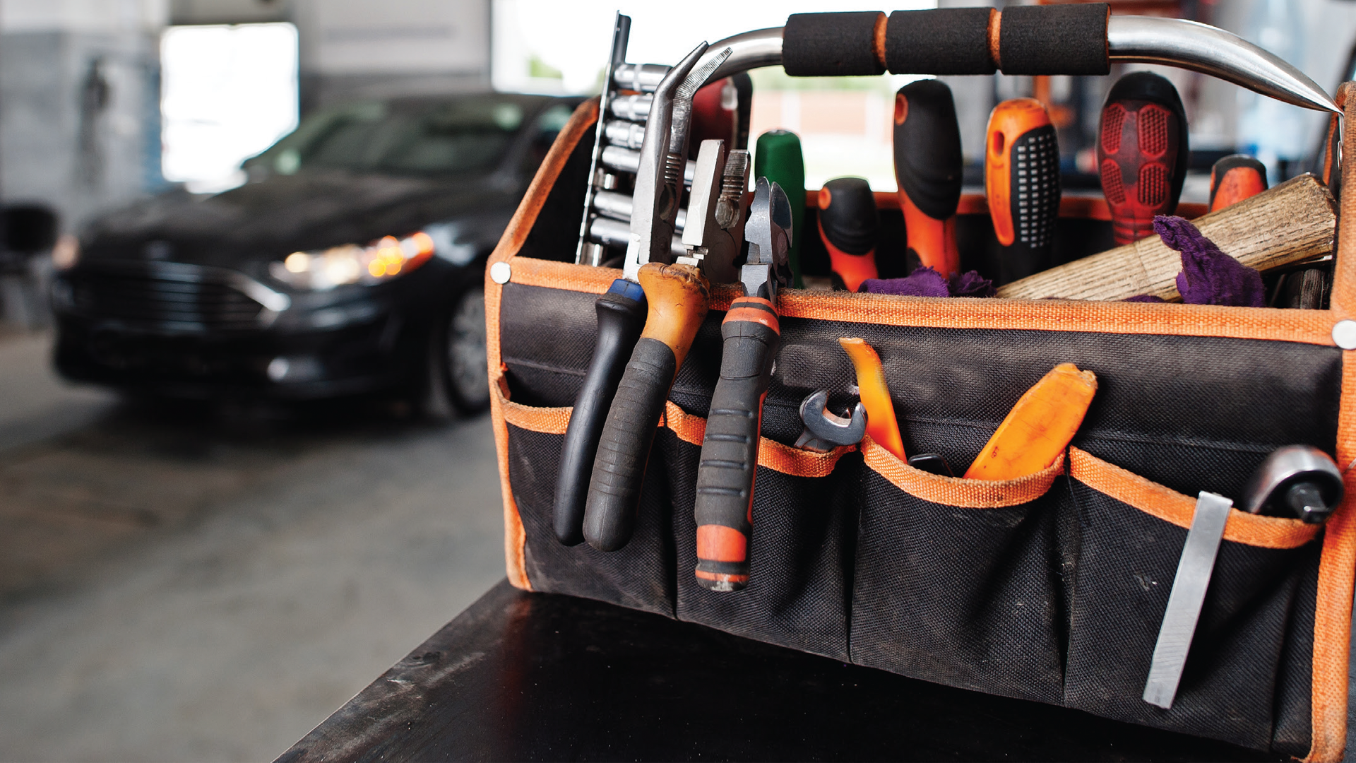 Orange and black tool bag with hand tools in automotive workshop
