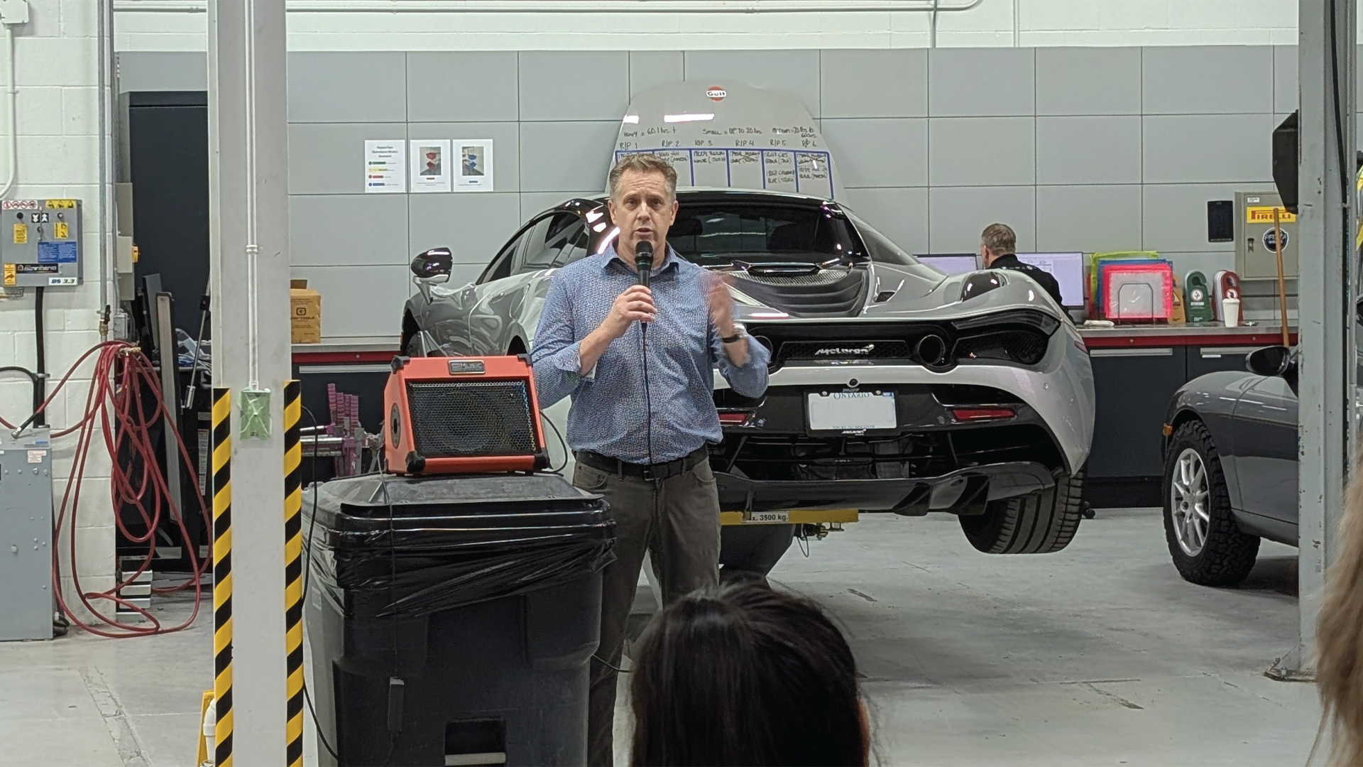 Person speaking with microphone in automotive workshop near high-end sports car