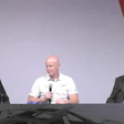 Three men seated at a panel discussion, holding microphones on a gray stage