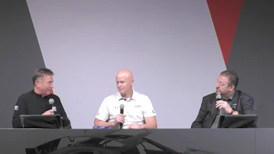Three men seated at a panel discussion, holding microphones on a gray stage