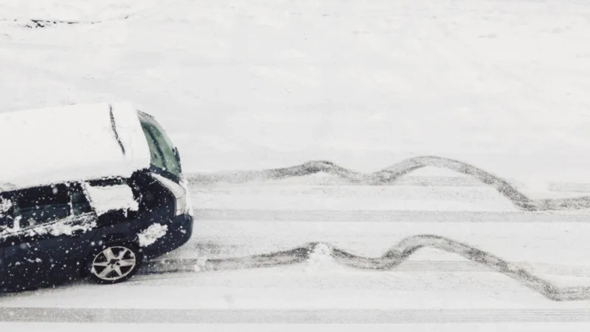 Dark car driving on snow-covered road with curved tire tracks