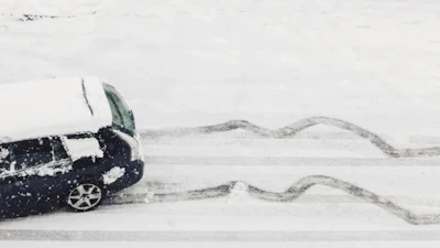 Dark car driving on snow-covered road with curved tire tracks