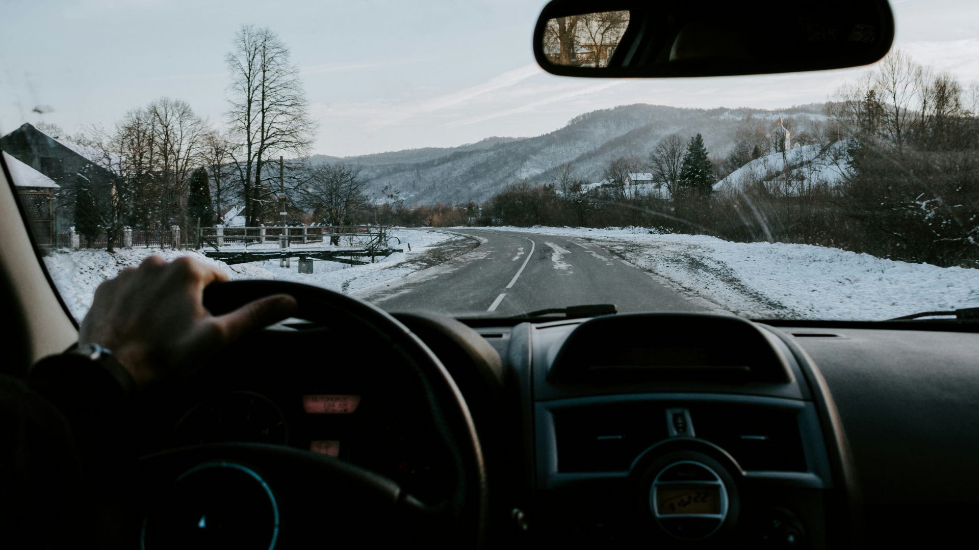 Driving on a snow-covered mountain road with winter landscape and hills in background