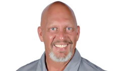 Smiling middle-aged bald man in gray polo shirt with company logo