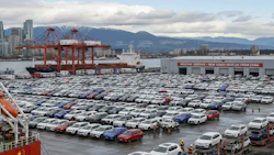 Cargo port with rows of new vehicles, shipping cranes, and mountains in background