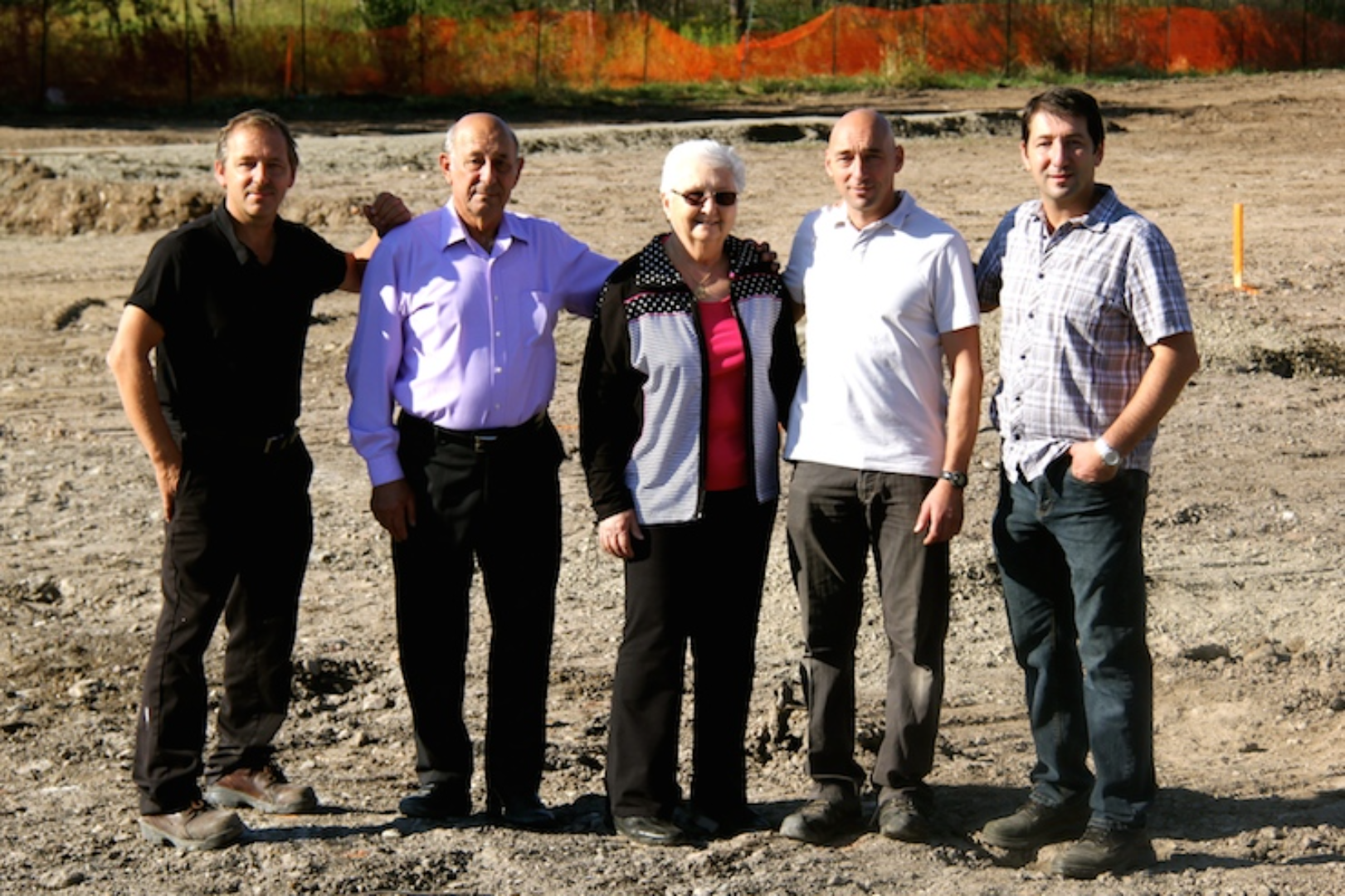 Five people standing together on a dirt construction site with orange fencing in background