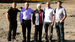 Five people standing together on a dirt construction site with orange fencing in background