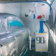 Auto body repair station with silver car in paint booth, equipment with '90e' label