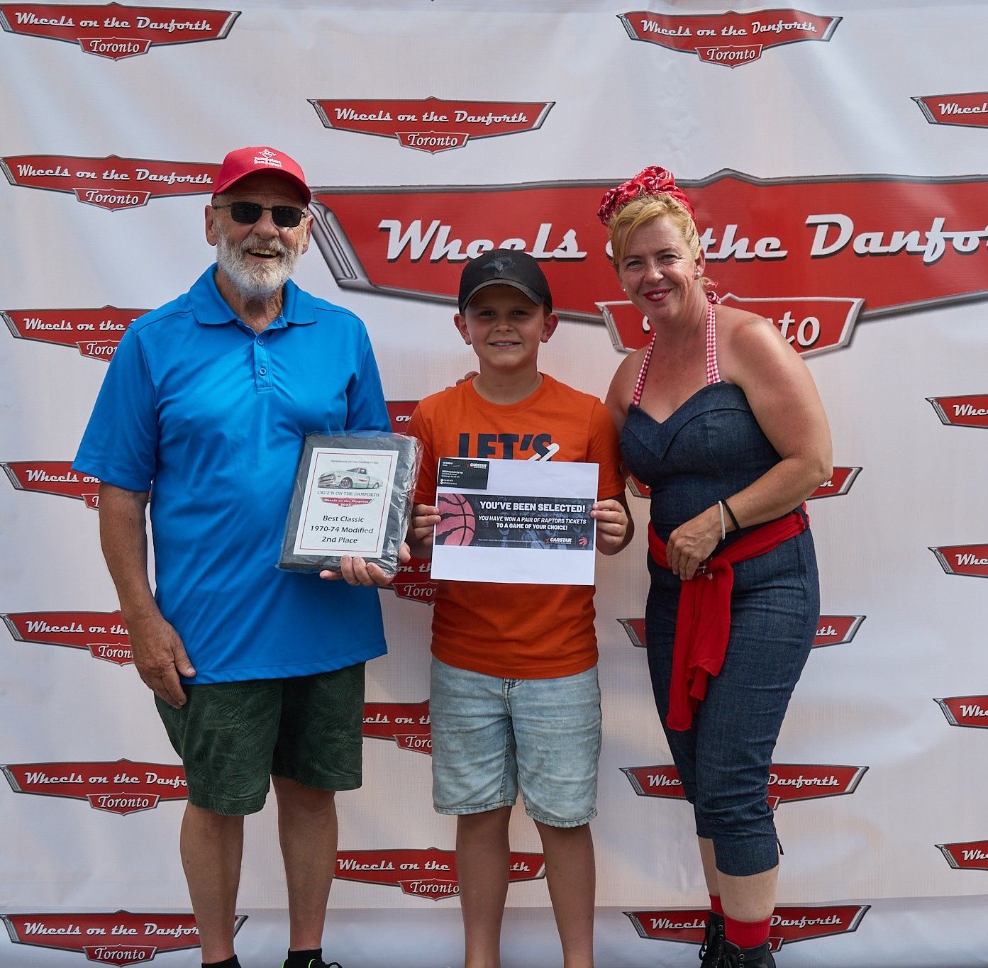 Three people posing at Wheels on the Danforth automotive event with branded backdrop