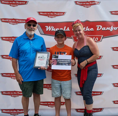 Three people posing at Wheels on the Danforth automotive event with branded backdrop