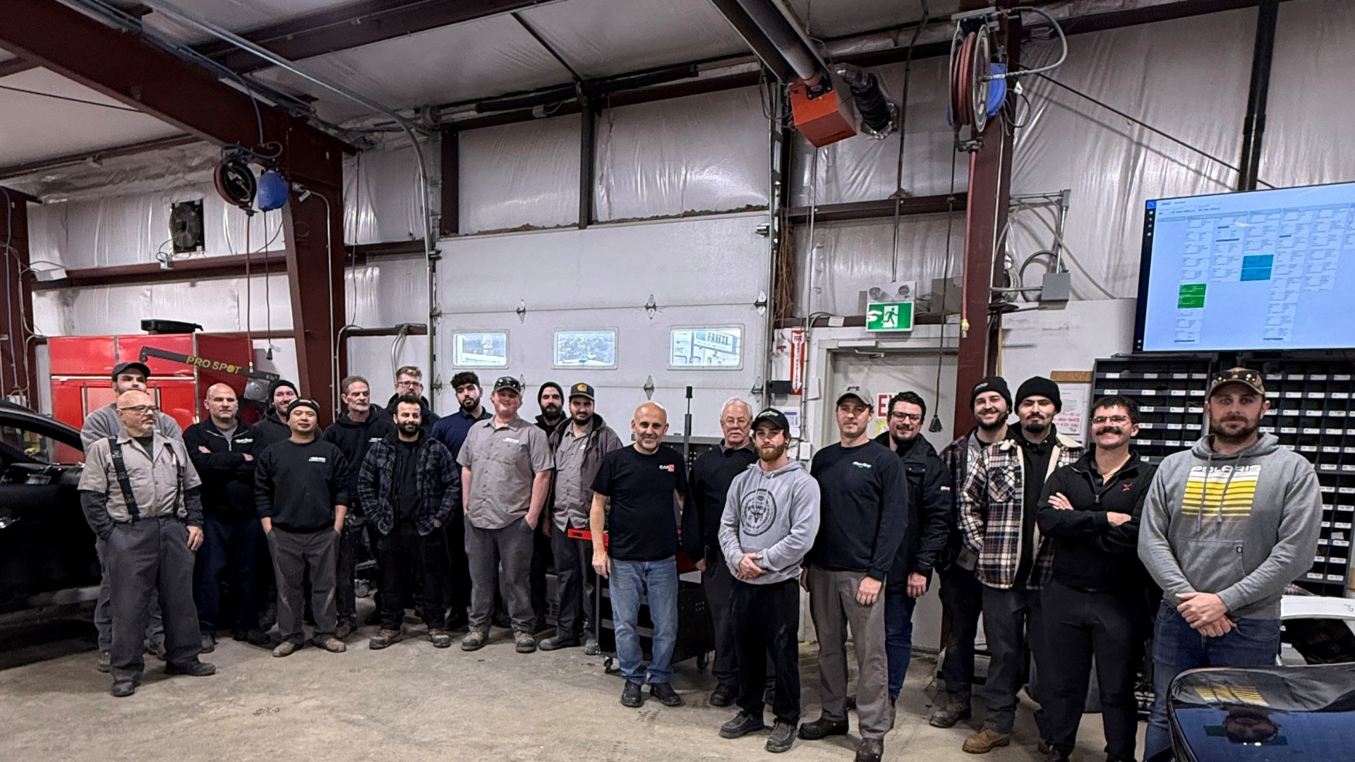Large group of technicians and workers posing together in an automotive repair workshop