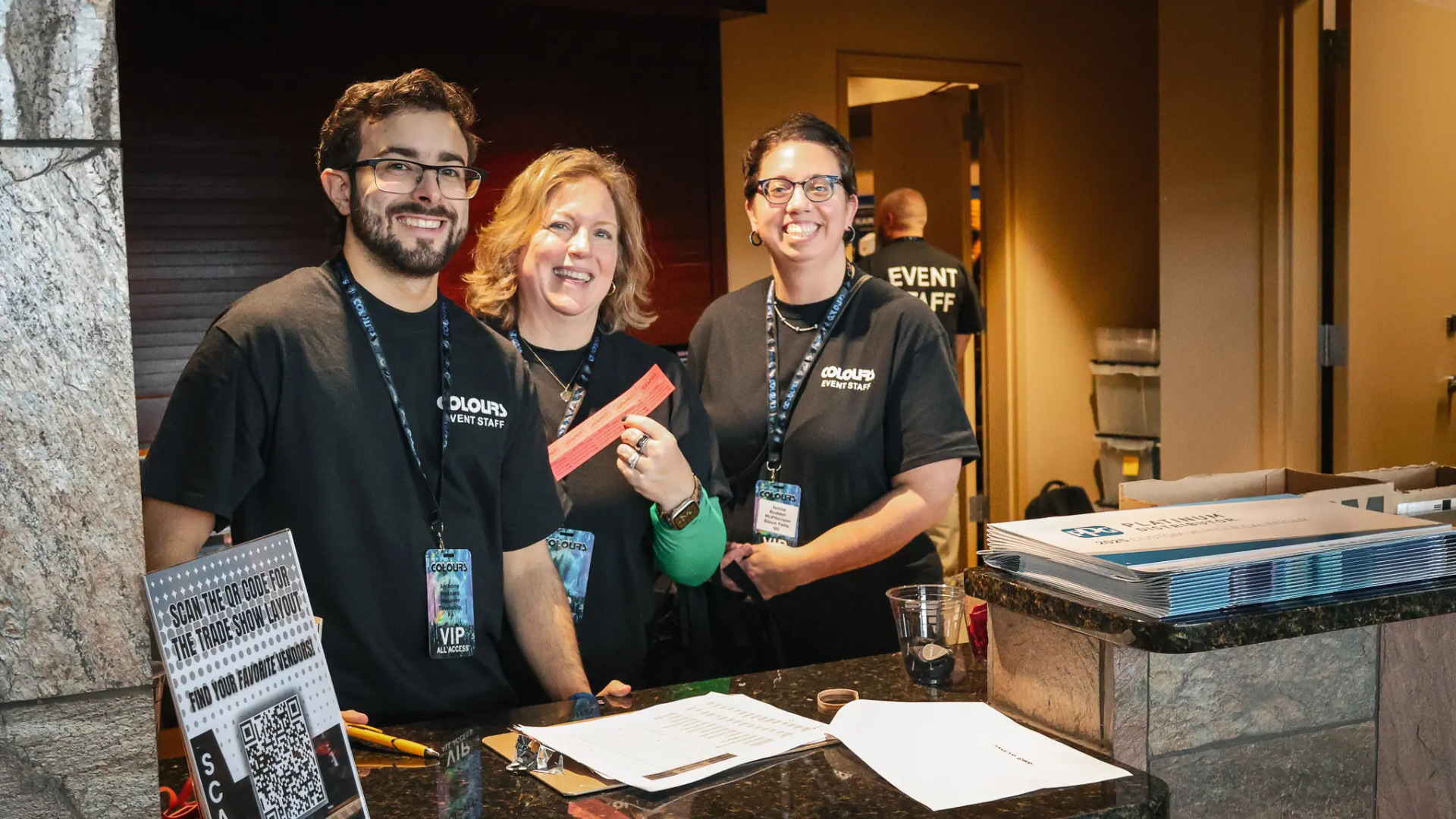 Three event staff members smiling behind a registration desk with event materials