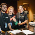 Three event staff members smiling behind a registration desk with event materials