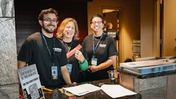 Three event staff members smiling behind a registration desk with event materials