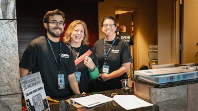 Three event staff members smiling behind a registration desk with event materials