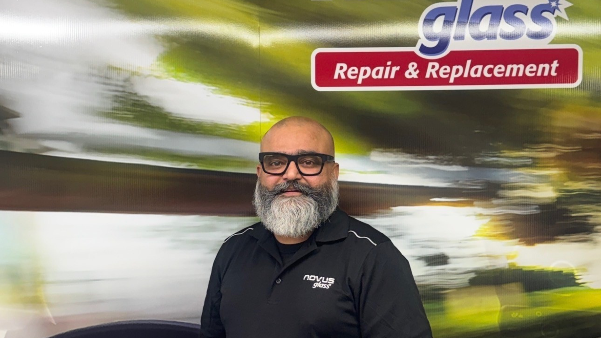 Bald professional with gray beard wearing Novus glass repair uniform