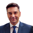 Professional man in navy suit and blue tie smiling against white background