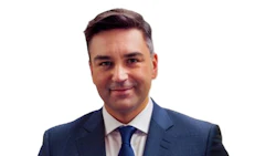 Professional man in navy suit and blue tie smiling against white background