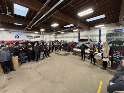 Automotive team meeting in repair shop with vehicles and BMW, Mercedes logos visible