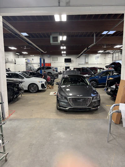 Auto repair shop interior with multiple vehicles and Genesis sedan in foreground
