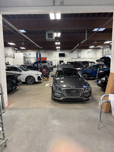Auto repair shop interior with multiple vehicles and Genesis sedan in foreground