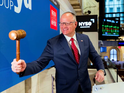 Smiling executive holding wooden gavel at NYSE trading floor