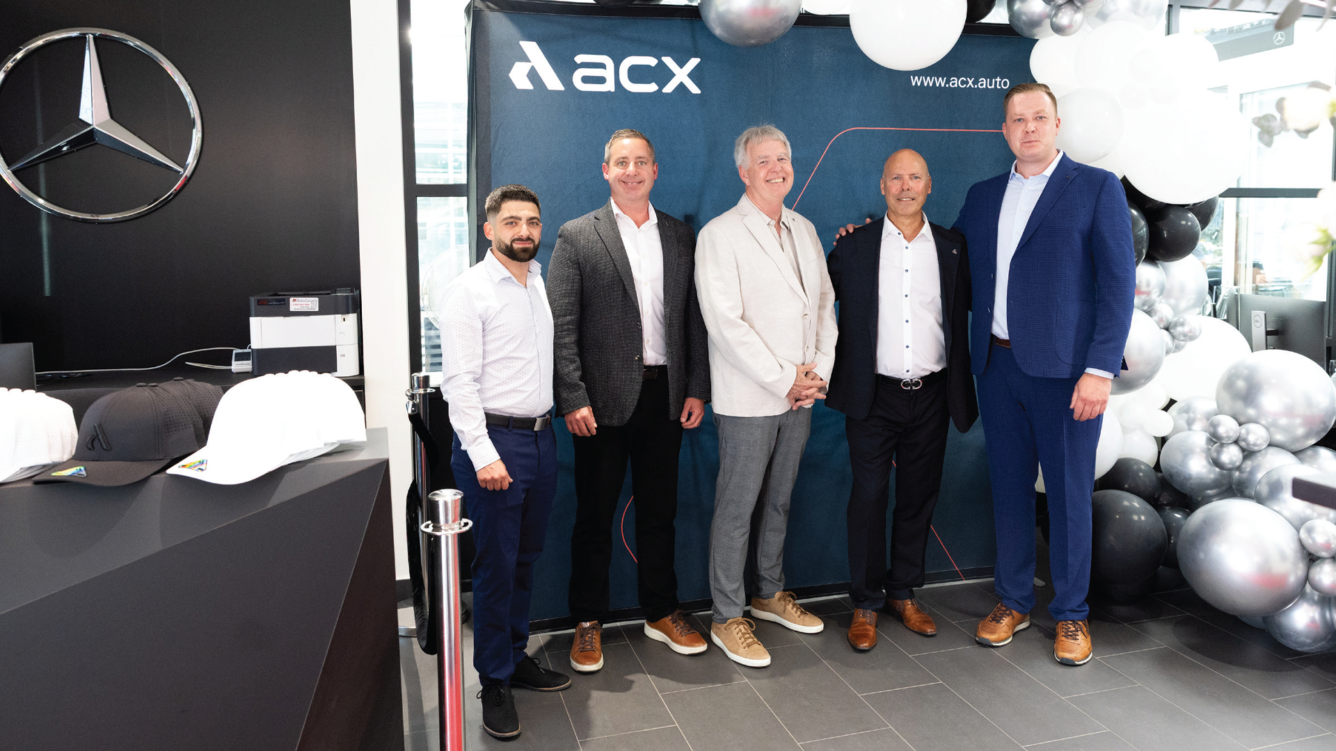 Five businessmen posing at Mercedes-Benz dealership with ACX event backdrop