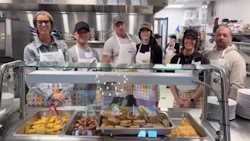 Kitchen staff standing behind food service counter with trays of prepared meals