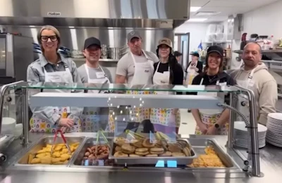Kitchen staff standing behind food service counter with trays of prepared meals